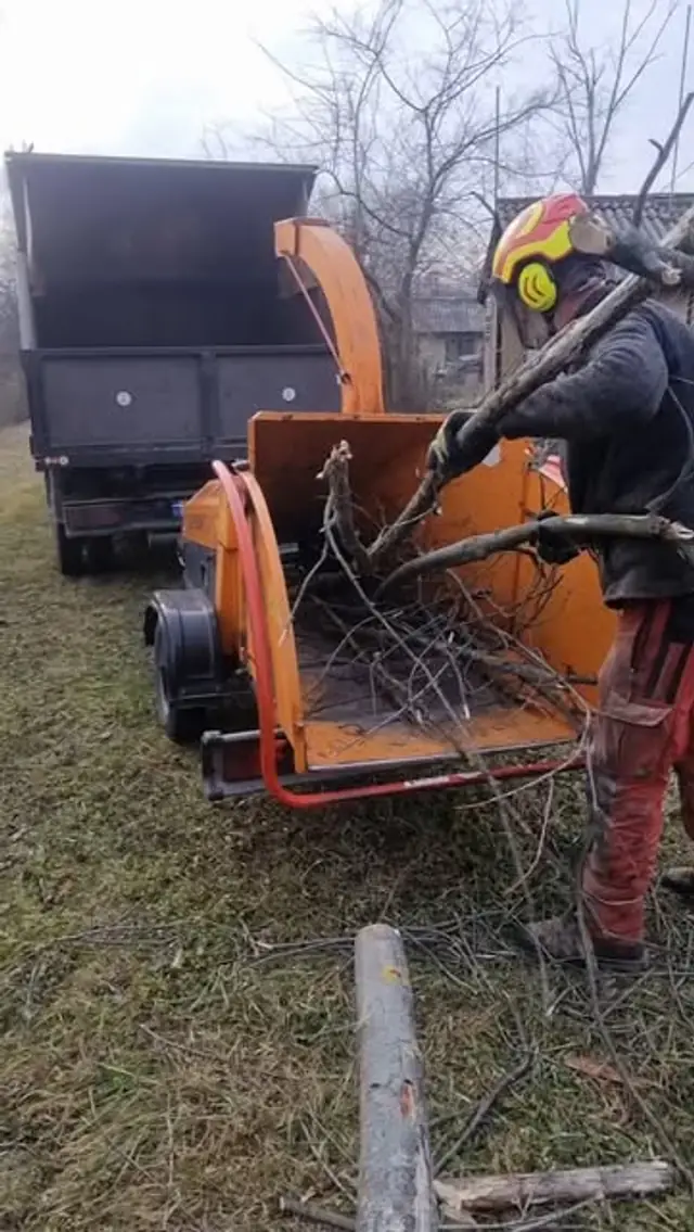 Narancssárga ágaprító gép, éppen ágakat adagolnak bele.